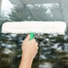 A person using an Unger green and white StripWasher to clean a window.