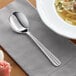 An Acopa Harmony stainless steel bouillon spoon on a napkin next to a bowl of soup.