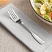 An Acopa Scottdale stainless steel salad fork on a napkin next to a bowl of salad.