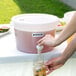 A person pouring liquid into a Choice white beverage dispenser on a table outdoors.