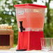 A red Choice 3 gallon beverage dispenser with glasses of juice.