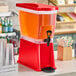 A red slim beverage dispenser filled with juice, featuring a spigot for easy pouring.