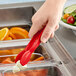 A hand using a Cambro red plastic tongs to serve salad over a container of food.