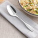 An Acopa Scottdale stainless steel dinner spoon on a napkin next to a bowl of food.