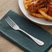 An Acopa Benson stainless steel table fork on a napkin next to a plate of food.