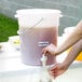 A person pouring purple juice into a white Choice round beverage dispenser.