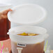 A hand using a white Choice beverage dispenser lid to pour brown liquid into a white container.