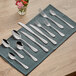 A group of Acopa Benson stainless steel forks on a table with a blue cloth and a napkin.