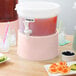 A pink and white Choice Rose round beverage dispenser base with a white lid and a straw in a glass.