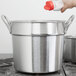 A hand pouring milk into a large silver double boiler inset.