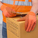 A person wearing Cordova hi-vis orange canvas work gloves with black PVC dots holding a box.