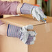 A person wearing Cordova striped canvas work gloves with leather palm coating and rubber cuffs cutting a box.