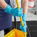 A person in blue Cordova Latex Rubber gloves holding a yellow mop handle.