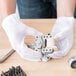 A person wearing Cordova Men's white and black nylon reversible inspection gloves holding a small metal object.