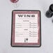 A burgundy menu with a marble border on a table with a glass of wine.