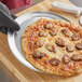 A person using a pizza peel to transfer a pizza from a pan to a plate.