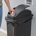 A person's hand putting a white tissue into a black Lavex trash can with a dome lid.