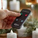 A person using a remote control to adjust Sterno Amber Rechargeable Flameless Tea Lights.