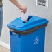 A woman putting paper into a blue Lavex slim rectangular recycling bin with a paper slot.