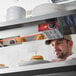 A man in a professional kitchen using an Avantco strip warmer to heat french fries on a white plate.