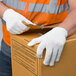 A pair of medium weight white polyester work gloves being worn while handling a cardboard box.