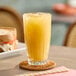 A glass of iced pineapple juice on a woven coaster.