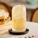 A glass of ginger ale with ice on a small black saucer.