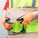 A person wearing Cordova Hi-Vis orange warehouse gloves with black foam nitrile coating holding a piece of wood.