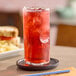 A tall glass of red cranberry juice with ice on a coaster.
