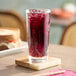 A tall glass of grape soda with ice on a coaster.