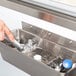 A hand using a Regency ice cream dipper well to wash an ice cream scoop.