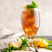 A glass of Narvon Lemon Sweet Iced Tea with a lemon wedge and mint leaves on the rim.