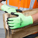 A person wearing Cordova Hi-Vis lime green gloves with black foam nitrile palm coating holding a piece of wood.