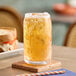A glass of iced cream soda on a coaster with a sandwich in the background.