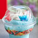 A clear plastic dome lid on a cup of frozen yogurt with cereal and whipped cream.