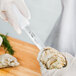 A person in gloves using a Choice Galveston Oyster Knife with a white handle to open an oyster.