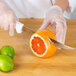 A person using a Choice serrated utility knife to cut an orange.