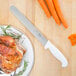 A Choice white straight edge slicing knife on a plate of food with turkey and carrots.