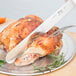 A Choice white straight edge slicing knife cutting a turkey on a plate.