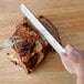 A hand holding a Choice slicing knife with a white handle cutting a piece of meat.