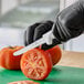 A serrated edge utility knife with a white handle being used to slice a tomato.