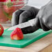 A small paring knife with a white handle being used to cut a strawberry on a green cutting board.