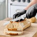 A serrated edge bread knife with a white handle being used to slice a loaf of bread.