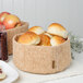 A Bambu cork fabric bowl filled with bread and fruit on a table in a bakery display.