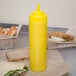 A yellow Choice wide mouth squeeze bottle on a table next to a sandwich.