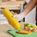 A yellow 24 oz. wide mouth squeeze bottle being used to dispense condiment onto a sandwich.