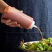 A person using a Choice clear squeeze bottle to pour sauce onto a salad.