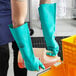 A person wearing Cordova green nitrile gloves and a green apron pouring liquid into a container.