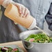 A person using a Choice wide mouth squeeze bottle to pour mustard onto a bowl of salad.