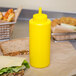 A yellow Choice squeeze bottle of mustard sits on a table next to a sandwich.